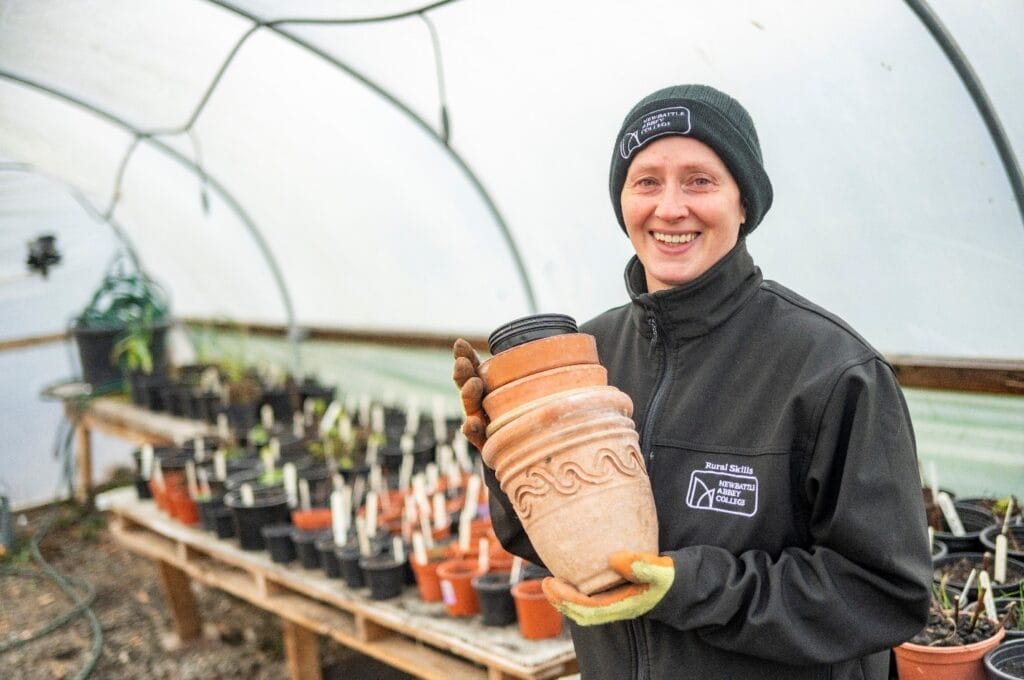 Lee Ryan of Newbattle Abbey College inside a greenhouse holding up a terracotta pot