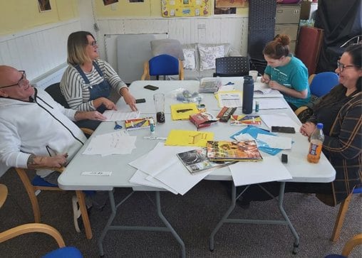 A group of adult learner sit around a table, which features various papers, stationery and drinks. The learners are benefitting from a learning programme that has gone through the credit rating process.