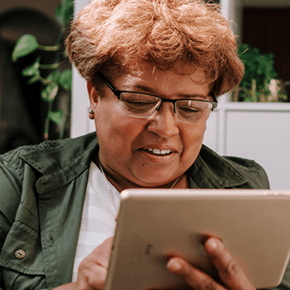 A mature learner sits outside surrounded by greenery. She's looking at an iPad and smiling. She signifies the learners that the SCQF helps.