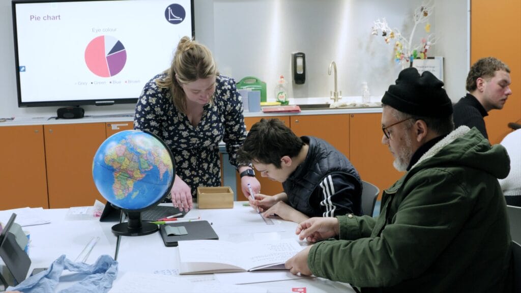 Learners taking part in the Adding Value course at Glasgow Science Centre. A teacher helps a young boy with his work while sitting at a desk