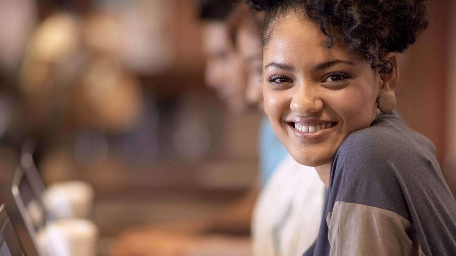 A young girl looks over her left shoulder at a camera while sitting at a laptop