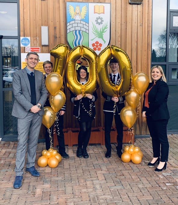 Staff and pupils from Denny High School holding gold ballooons 1-0-0 outside the school entrance