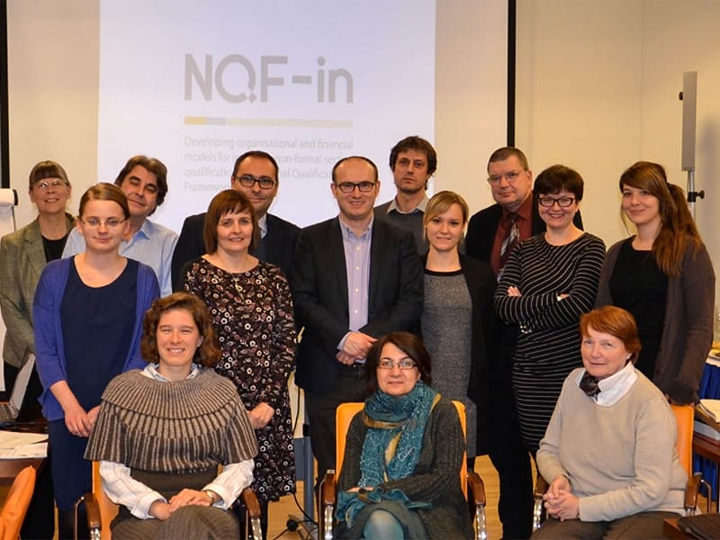Group of delegates at the NQF-in Project Kick-off meeting standing and sitting in a classroom in Warsaw, Poland