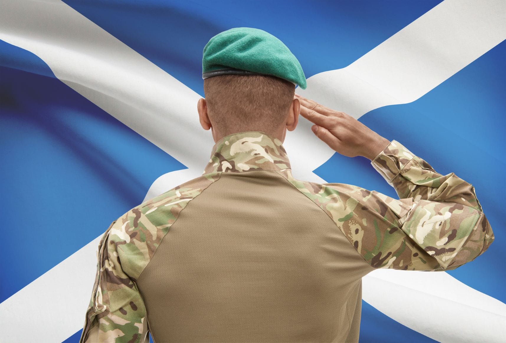 Marine with his back to the camera saluting the St Andrew's Cross flag