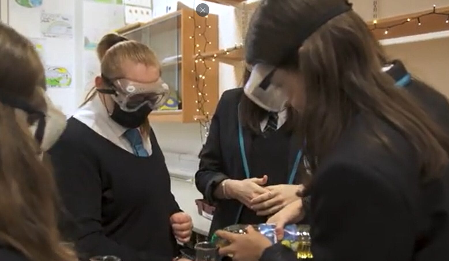 Senior high school pupils wearing eye protection, gathered around a science experiment