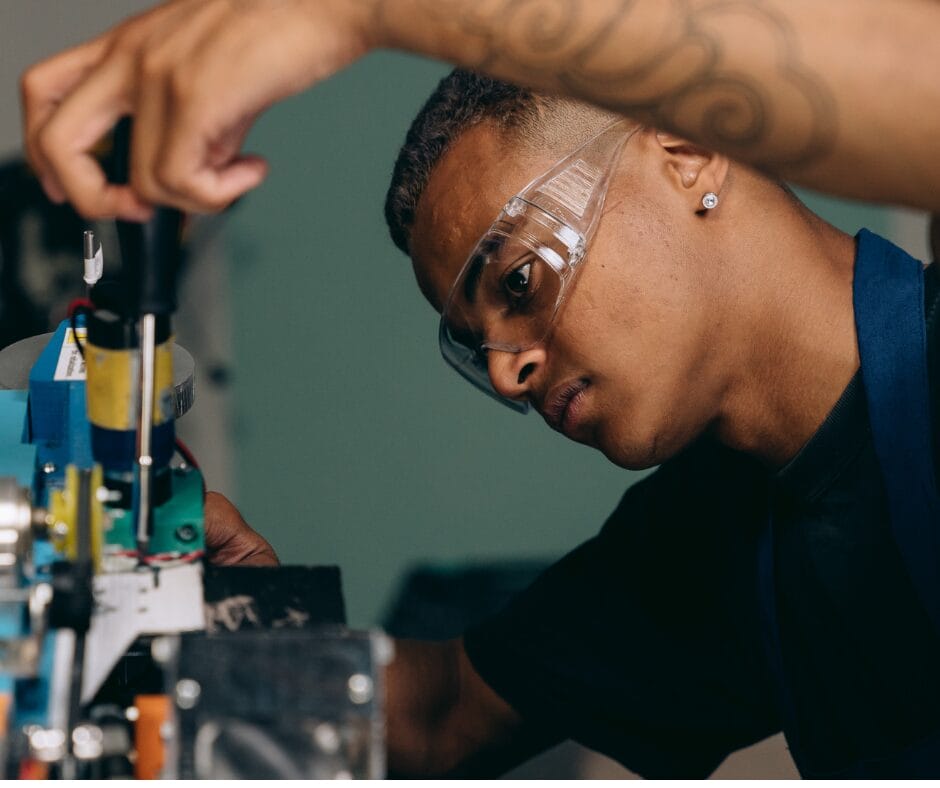 Man in safety goggles examines mechanical equipment, while working on the equipment with a screwdriver. He represents an apprenticeship