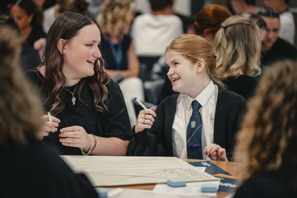 An adult and a school pupil in uniform, smiling at each other, sitting at a table